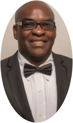 Professional headshot of man in tuxedo with bow tie and glasses, smiling at camera